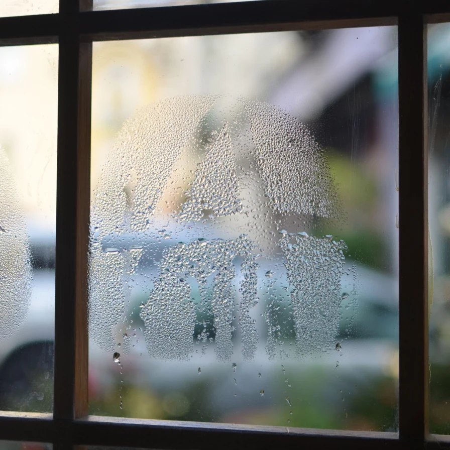 Cristal de una ventana empañado por la condensación, con una calle desenfocada al fondo