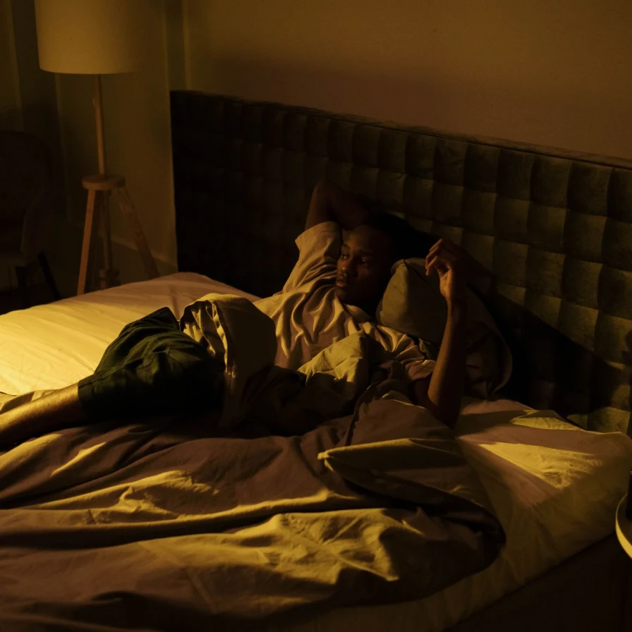 Hombre despierto tumbado en la cama, en una habitación de noche con luz cálida tenue