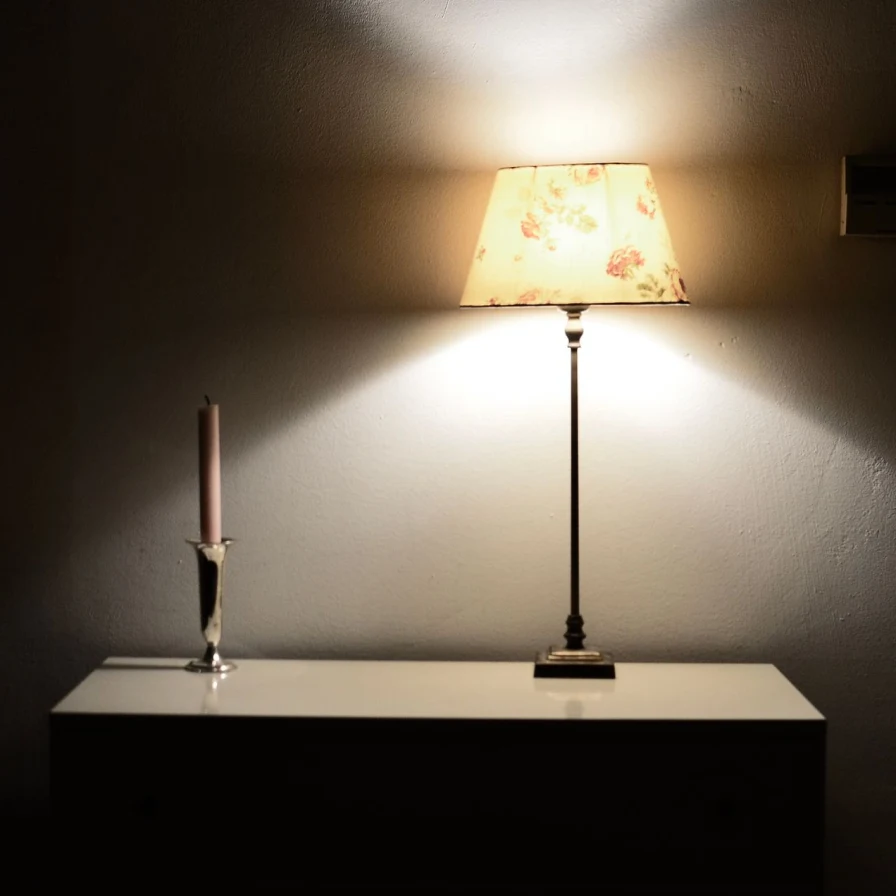 Lámpara de mesa encendida junto a una vela sobre una cómoda
