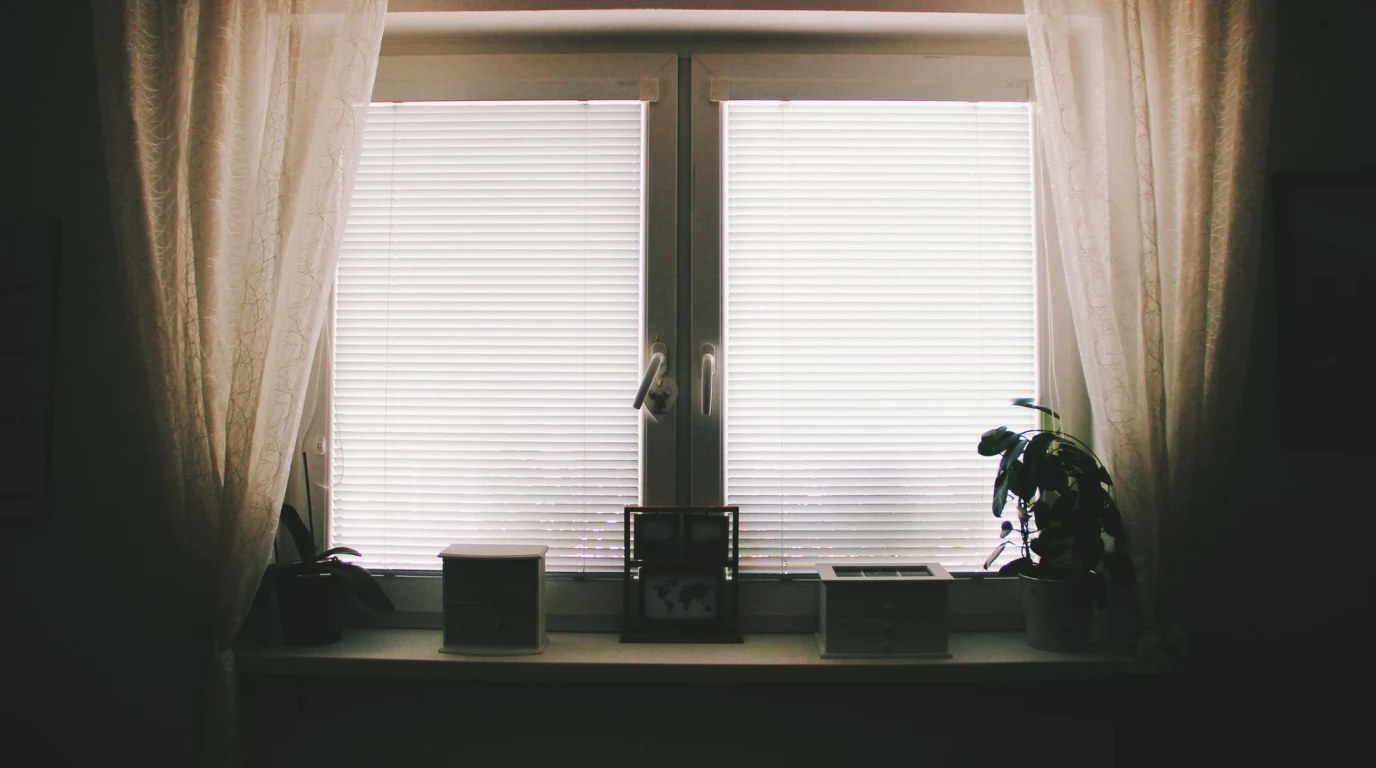 Ventana con persianas y cortinas por la que entra una luz suave