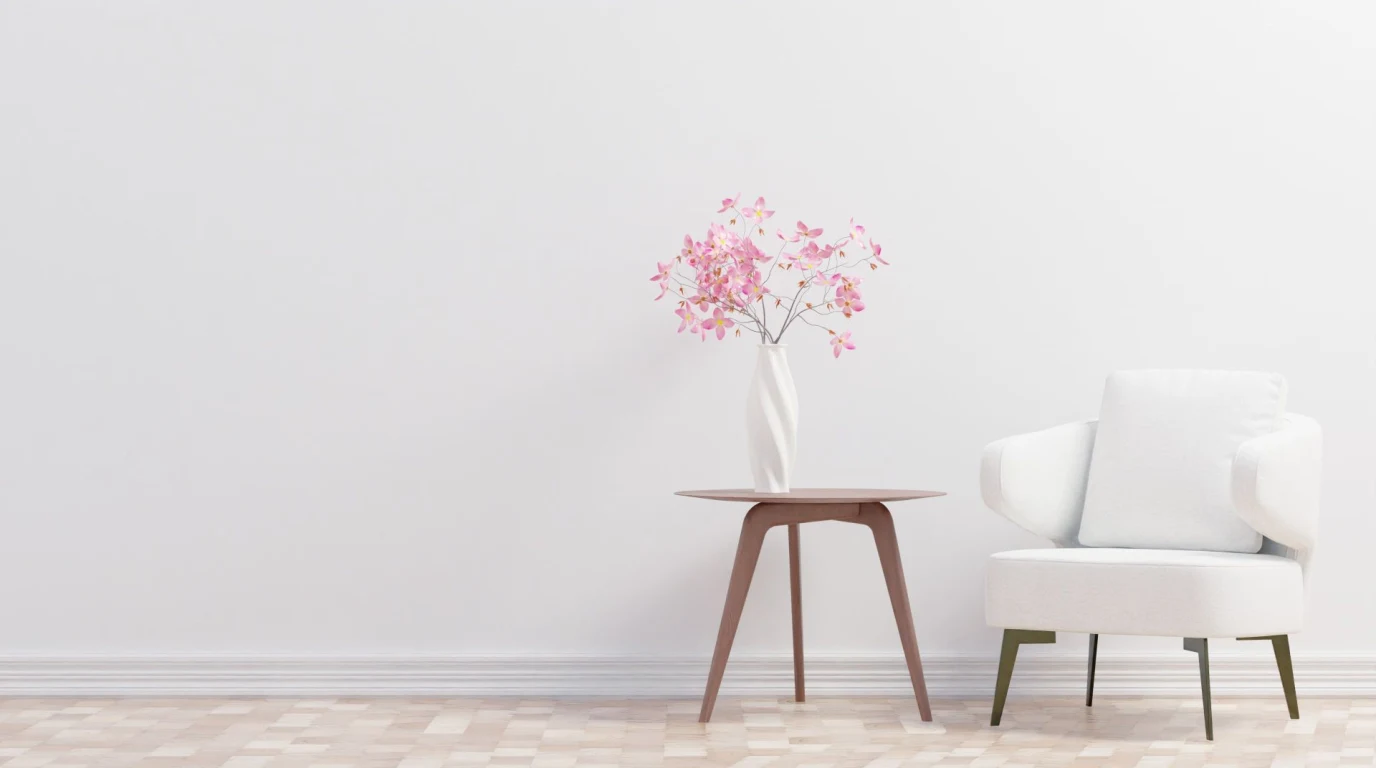Salón luminoso con una butaca blanca y una mesita con un jarrón de flores rosas