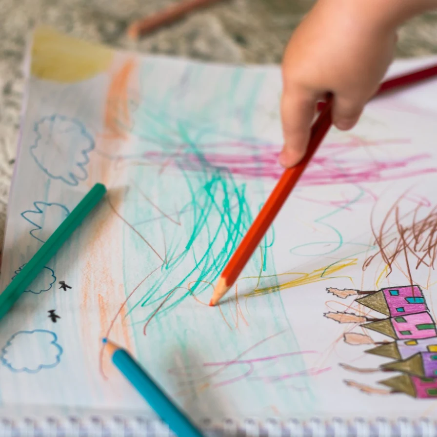 Mano de un niño dibujando con un lápiz de color sobre un dibujo de casas