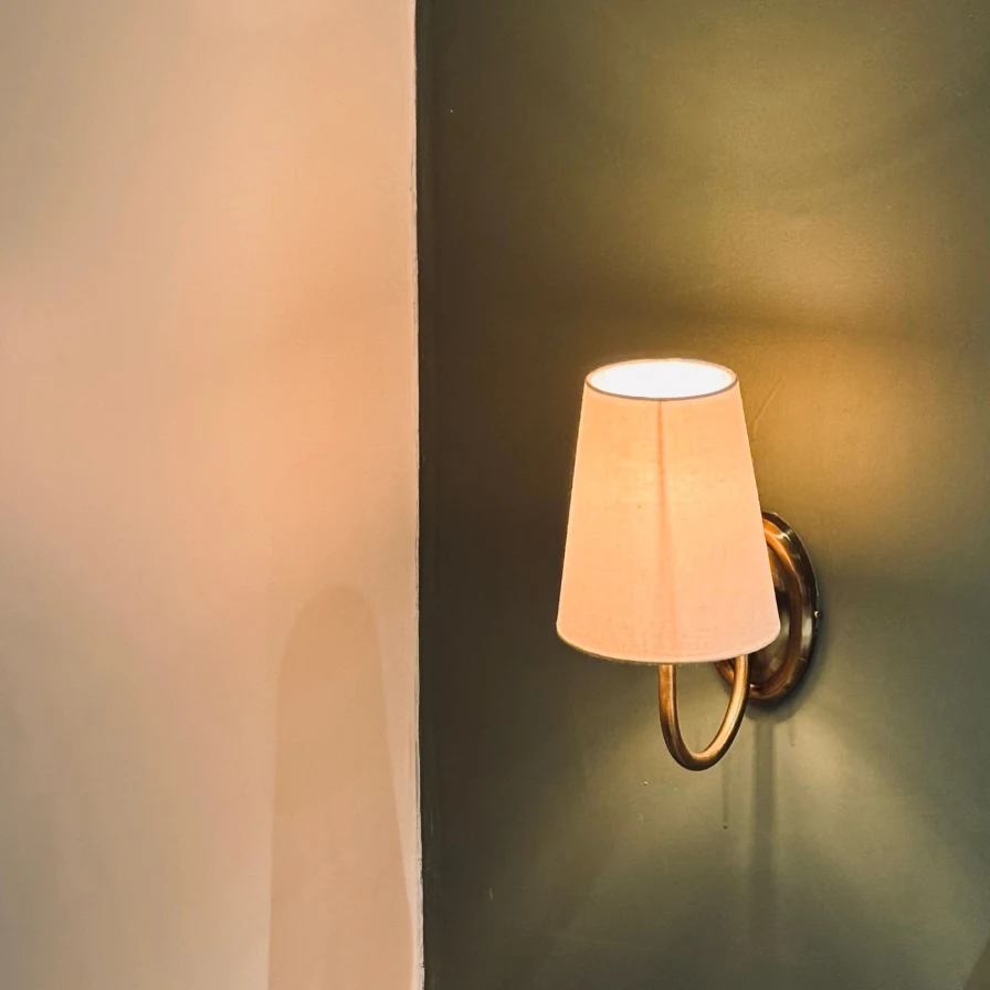 Aplique de pared encendido con pantalla de tela, que proyecta una luz cálida sobre una pared verde
