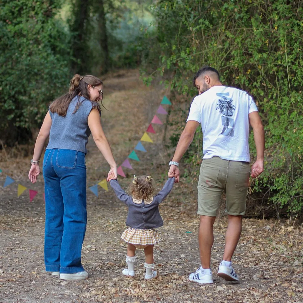 Fotografía: una pareja y su hija pequeña caminan de la mano por un sendero entre árboles