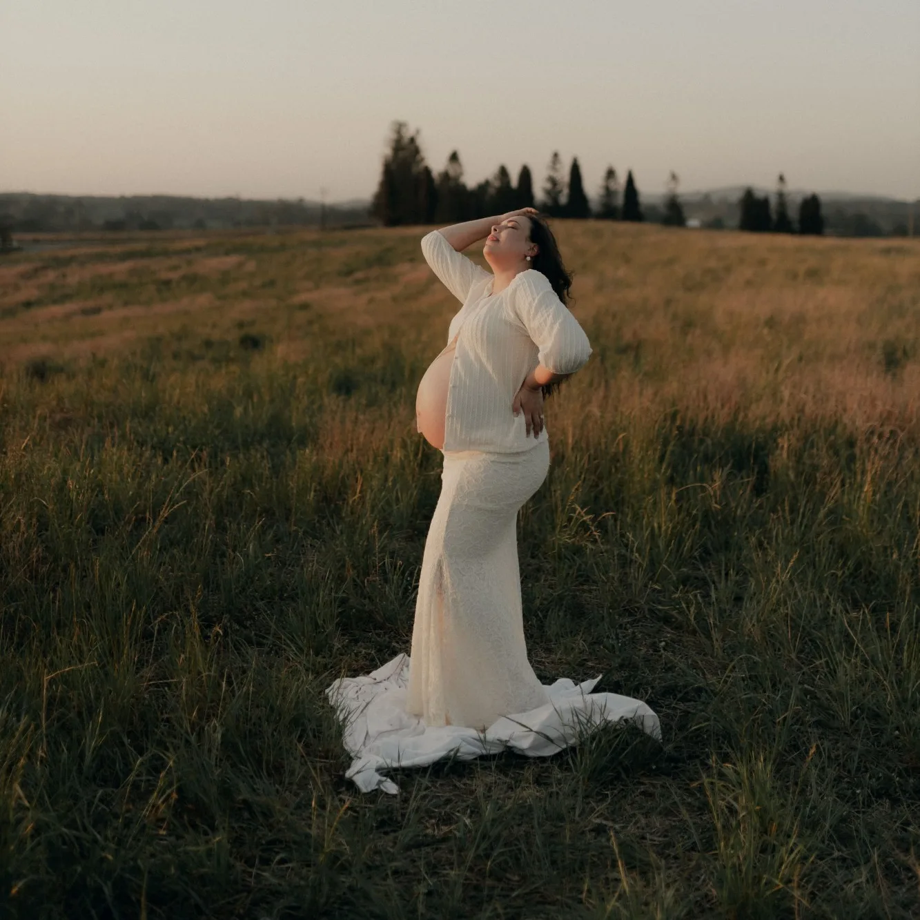 Fotografía: una mujer embarazada, de pie en un prado al atardecer