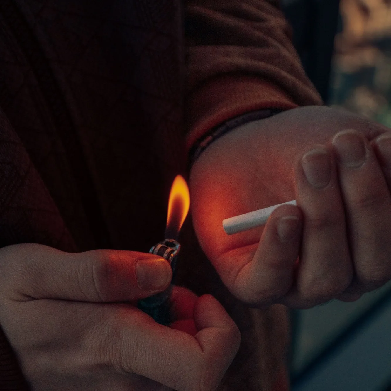 Fotografía: unas manos encienden un cigarrillo con un mechero en la penumbra